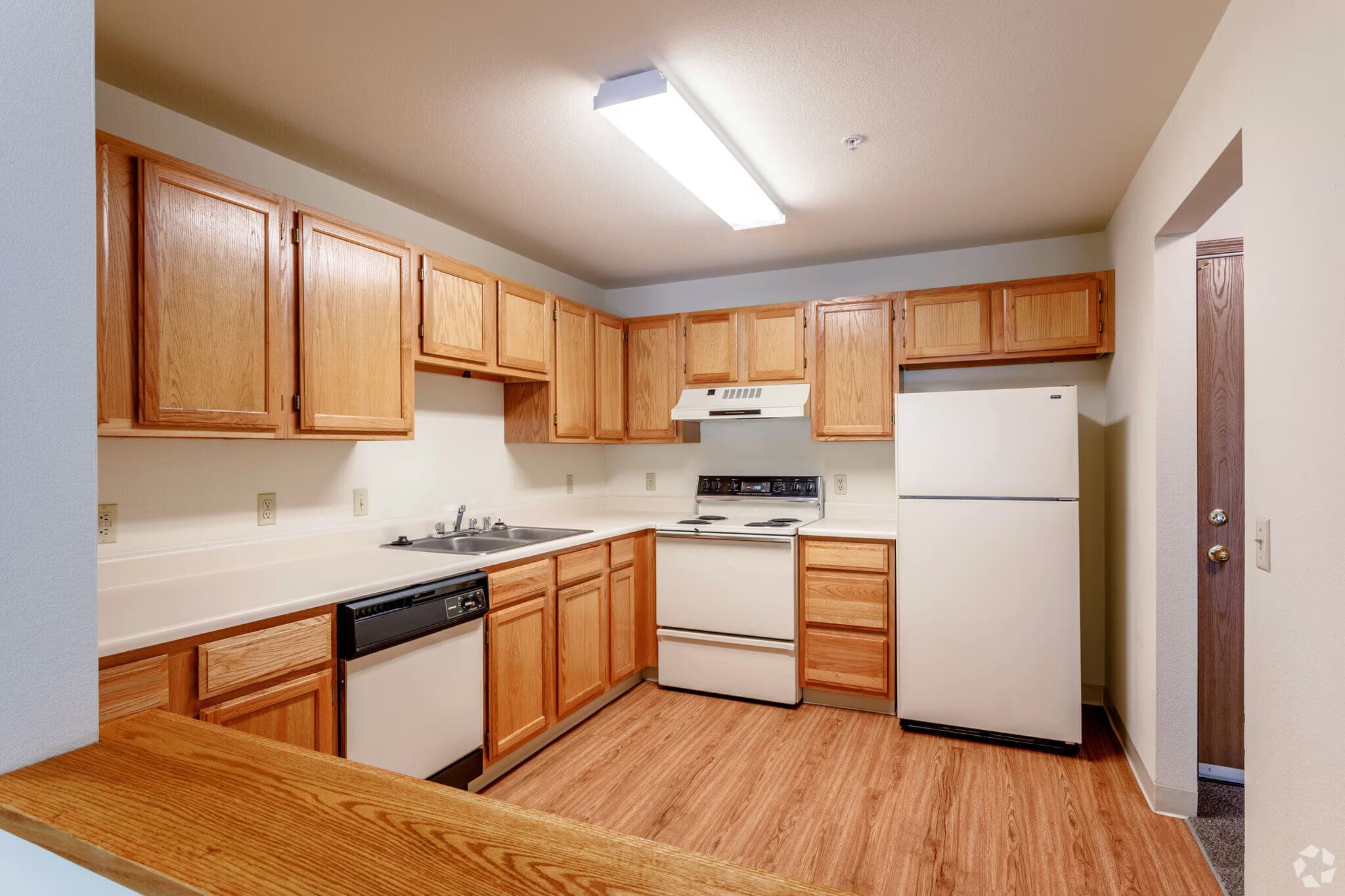 A kitchen with oak cabinets, an electric range, dishwasher, full-size refrigerator, double-basin sink and a breakfast bar.