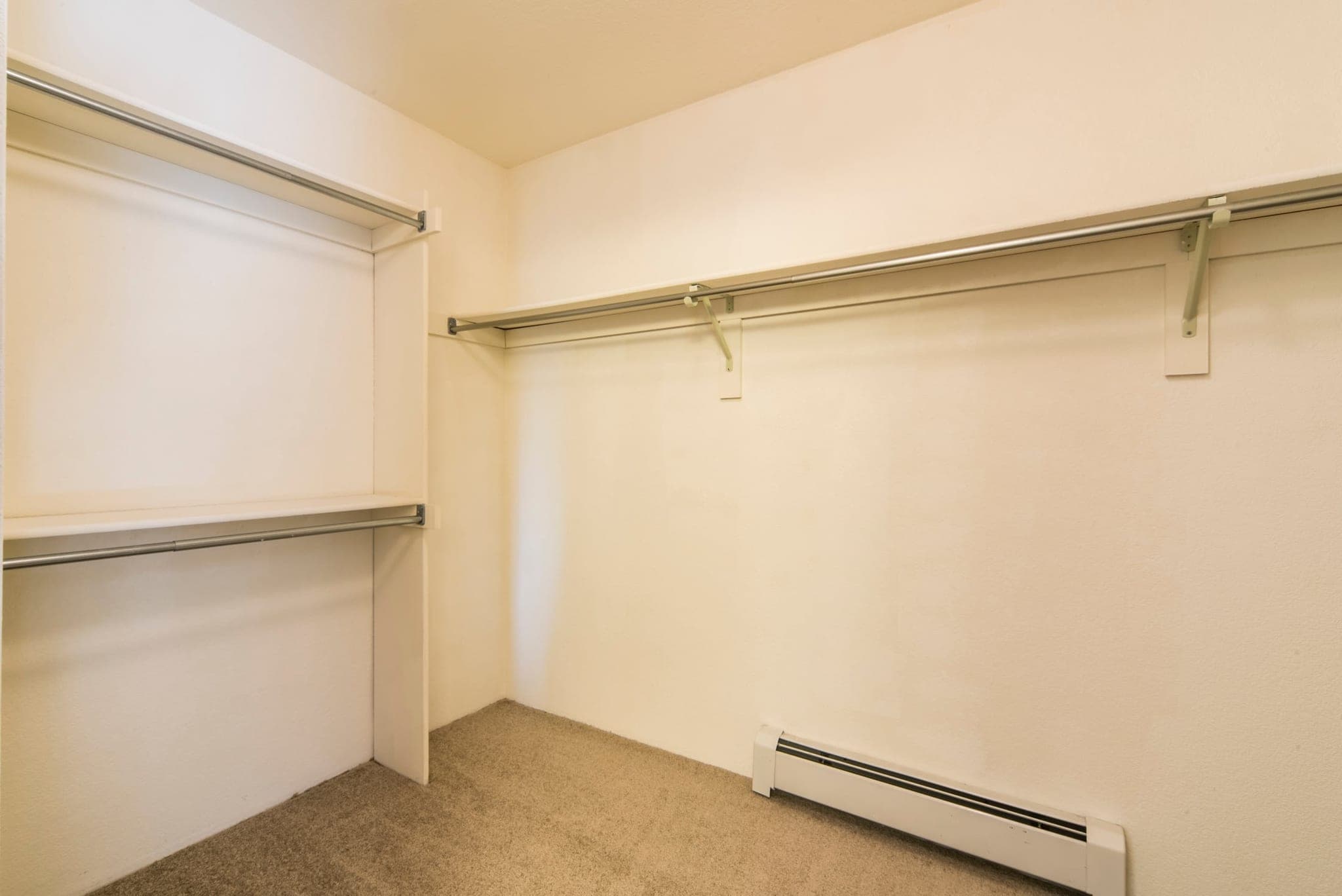 An empty walk-in closet, wide enough to stand inside, with hanging rails at two heights down one wall and a shelf above each.